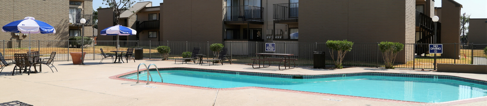 Outdoor community pool at an apartment complex with lounge chairs, tables, and blue umbrellas at Brookview, offering apartments in Odessa, TX.