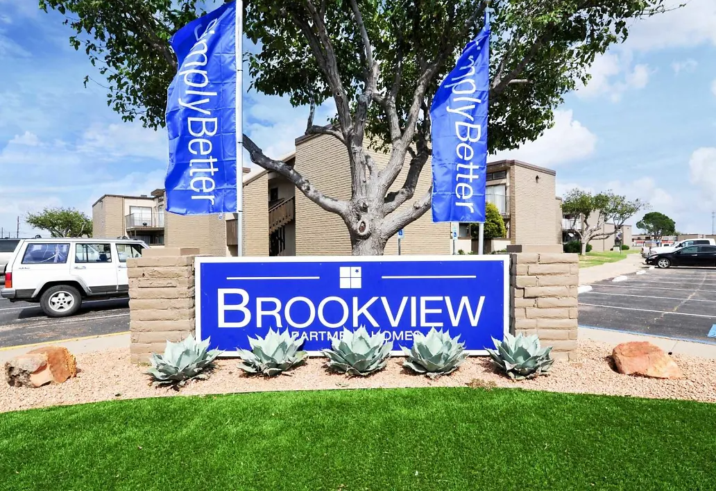 Blue Brookview Apartments sign at the community entrance with flags and desert landscaping.
