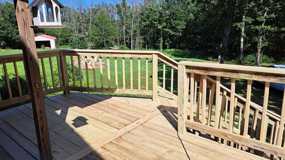 Wooden deck with railing overlooking a grassy yard and trees on a sunny day.