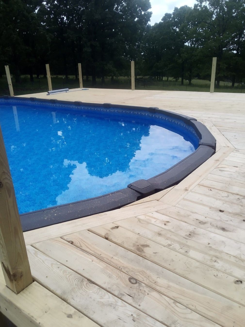 Above ground pool with a wooden deck, surrounded by trees.