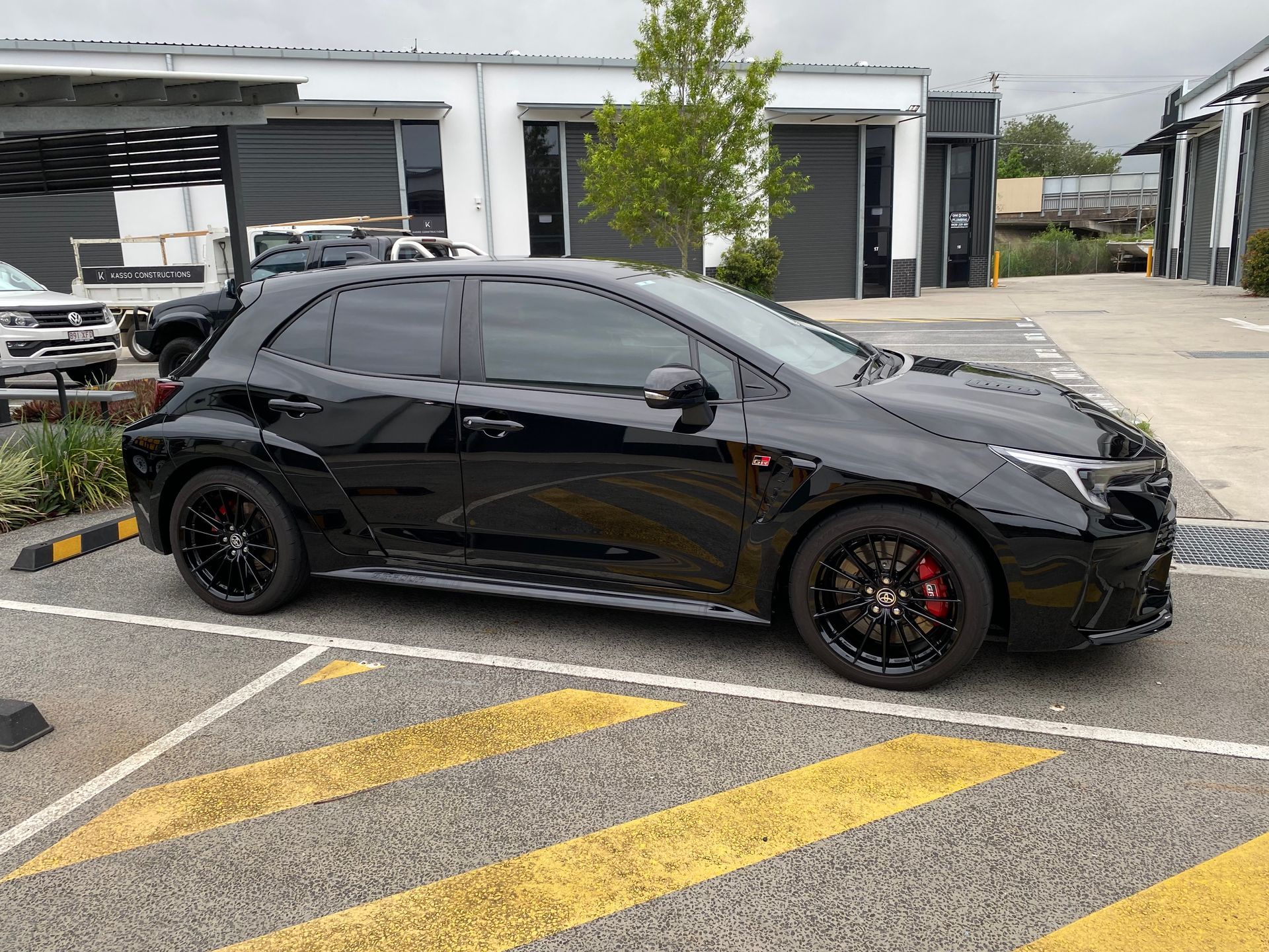 A black car is parked in a parking lot in front of a building.