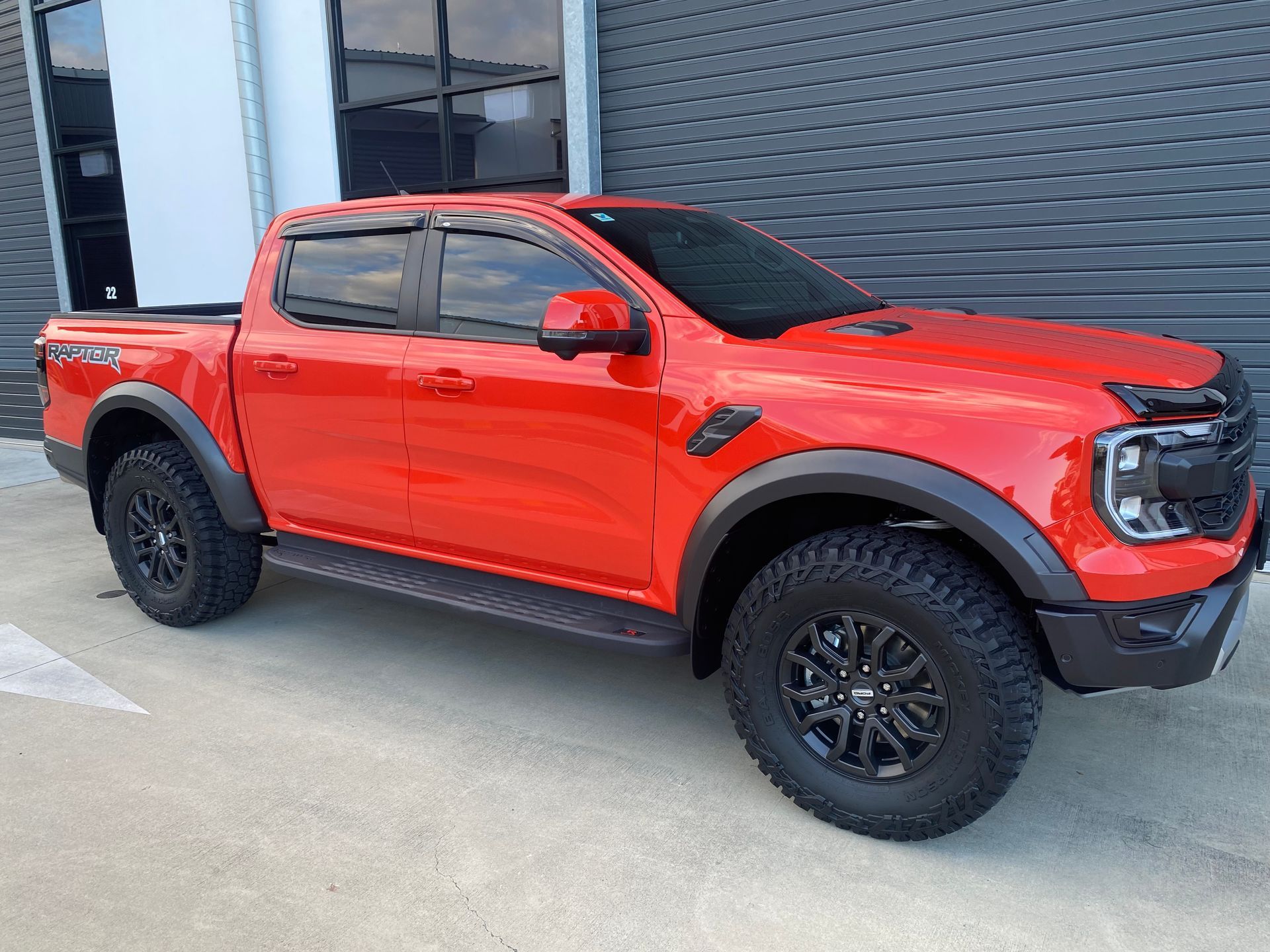 A red ford ranger raptor is parked in front of a building.