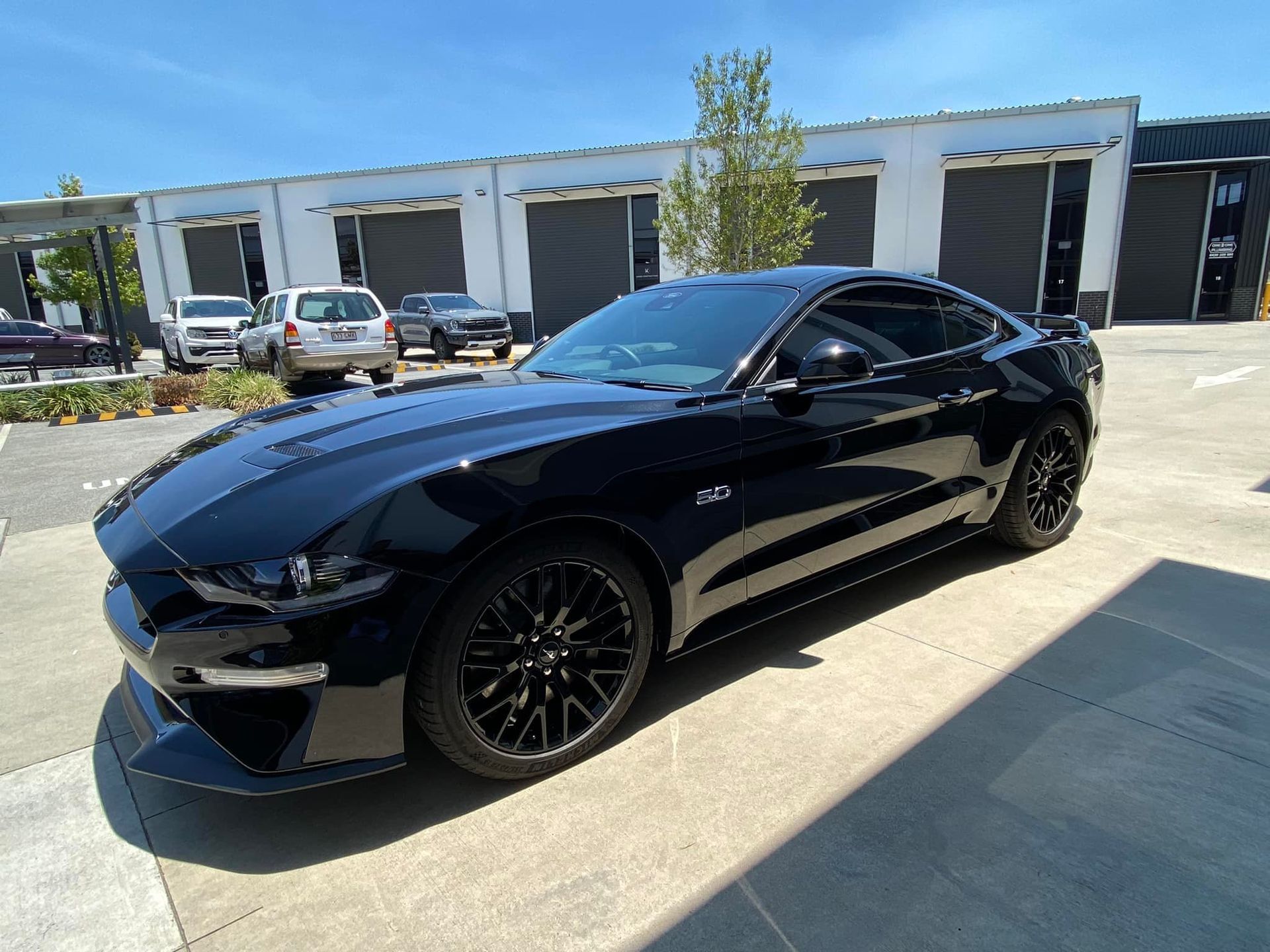 A black ford mustang is parked in a parking lot in front of a building.