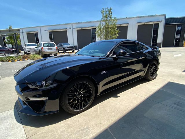 A black ford mustang is parked in a parking lot in front of a building - window tinting by Tint Wright Brisbane