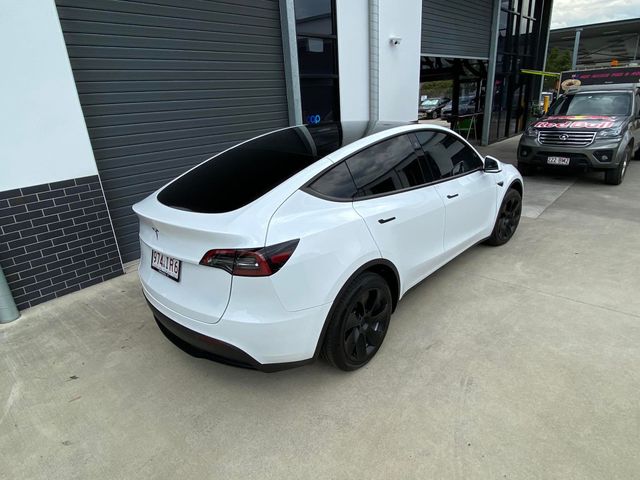 A white tesla model y is parked in front of a building - window tinting by Tint Wright Brisbane