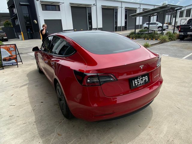 A red tesla model 3 is parked in a parking lot - window tinting by Tint Wright Brisbane