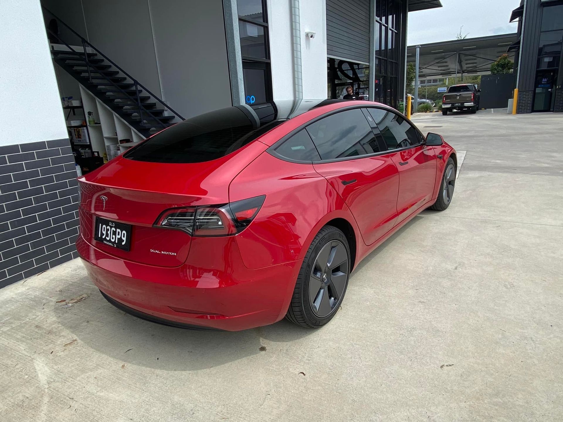 A red tesla model 3 is parked in front of a building.