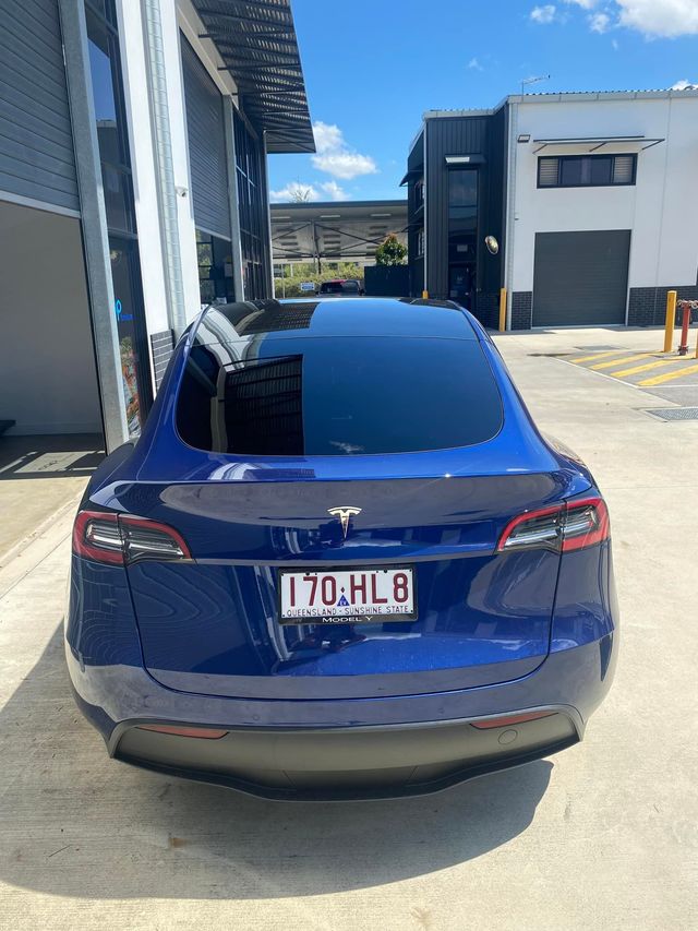 A blue tesla model 3 is parked in front of a building - window tinting by Tint Wright Brisbane