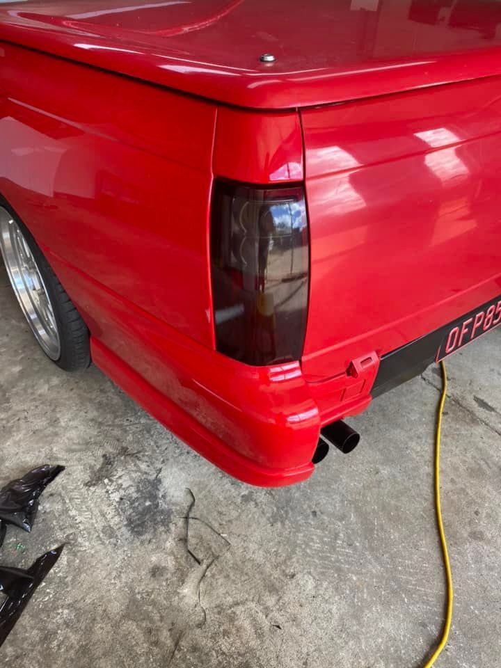 A red truck with a black tail light is parked in a garage.