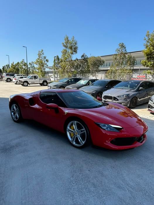 A red ferrari is parked in a parking lot next to other cars.