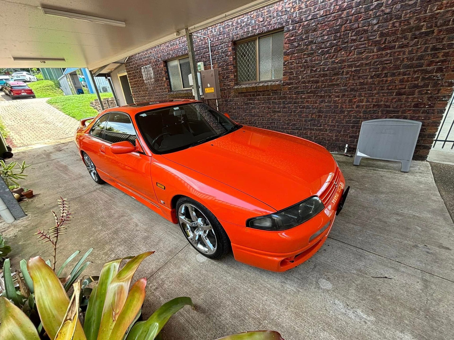 An orange car is parked in front of a brick building.