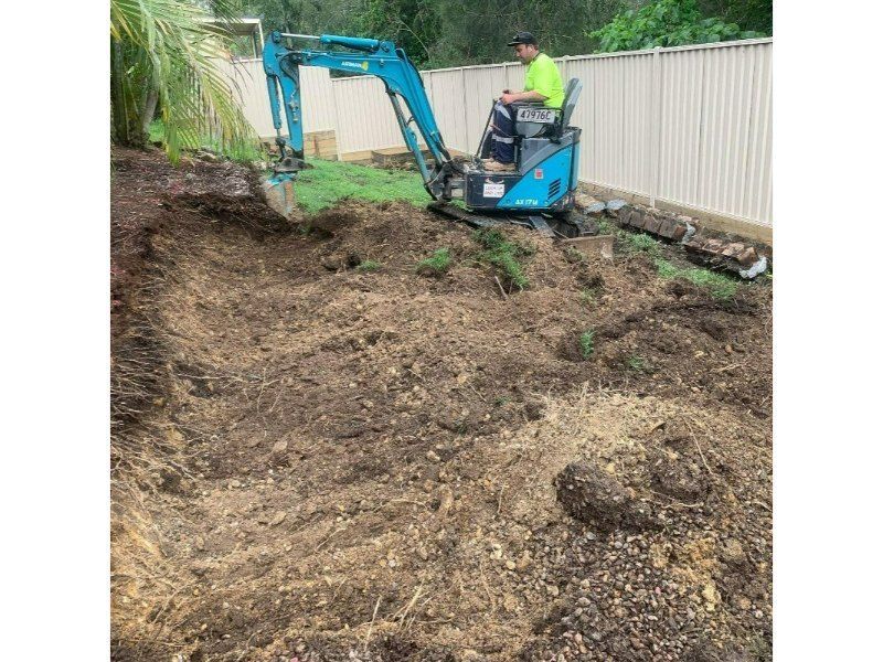 A Man is Driving a Small Excavator in a Dirt Field — Turnscape Landscaping In Broadbeach, QLD