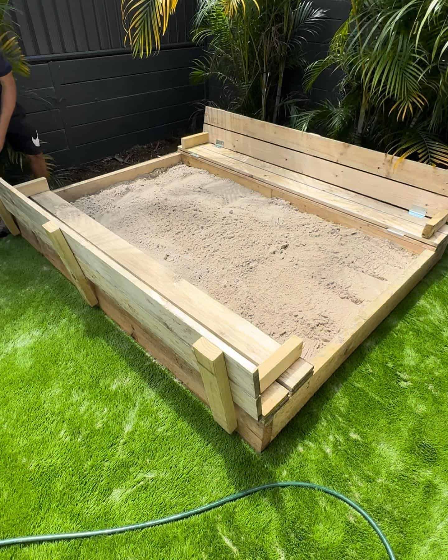 A wooden sandbox is sitting on top of a lush green lawn. — Turnscape Landscaping in Mudgeeraba, QLD