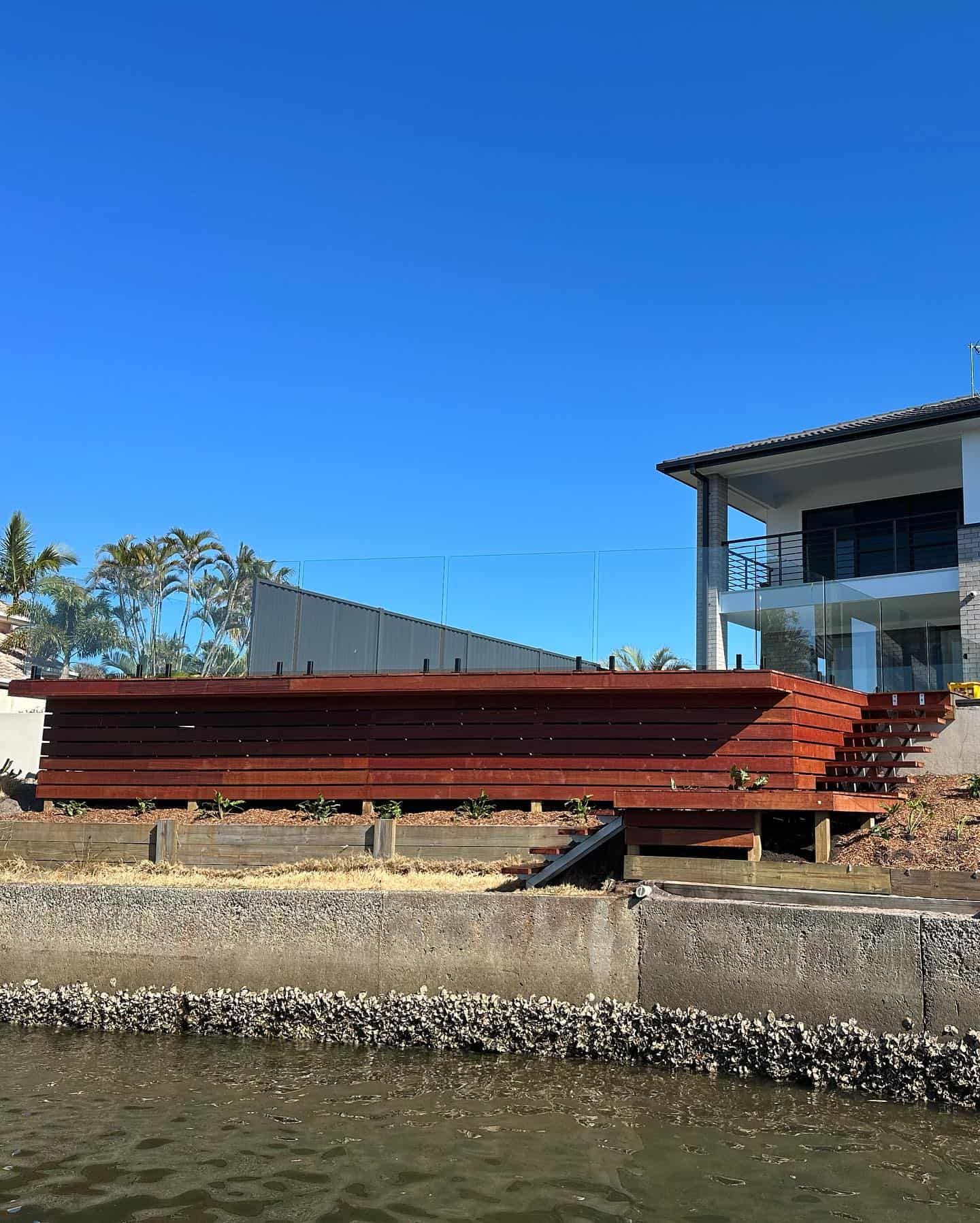 A large wooden structure is sitting next to a large house next to a body of water. — Turnscape Landscaping In Broadbeach, QLD