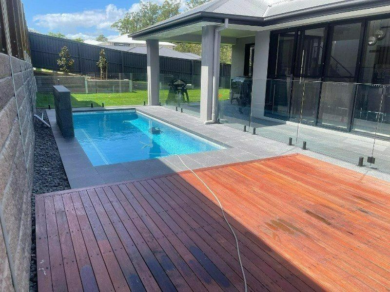 A swimming pool in the backyard of a house with a wooden deck — Turnscape Landscaping In Broadbeach, QLD