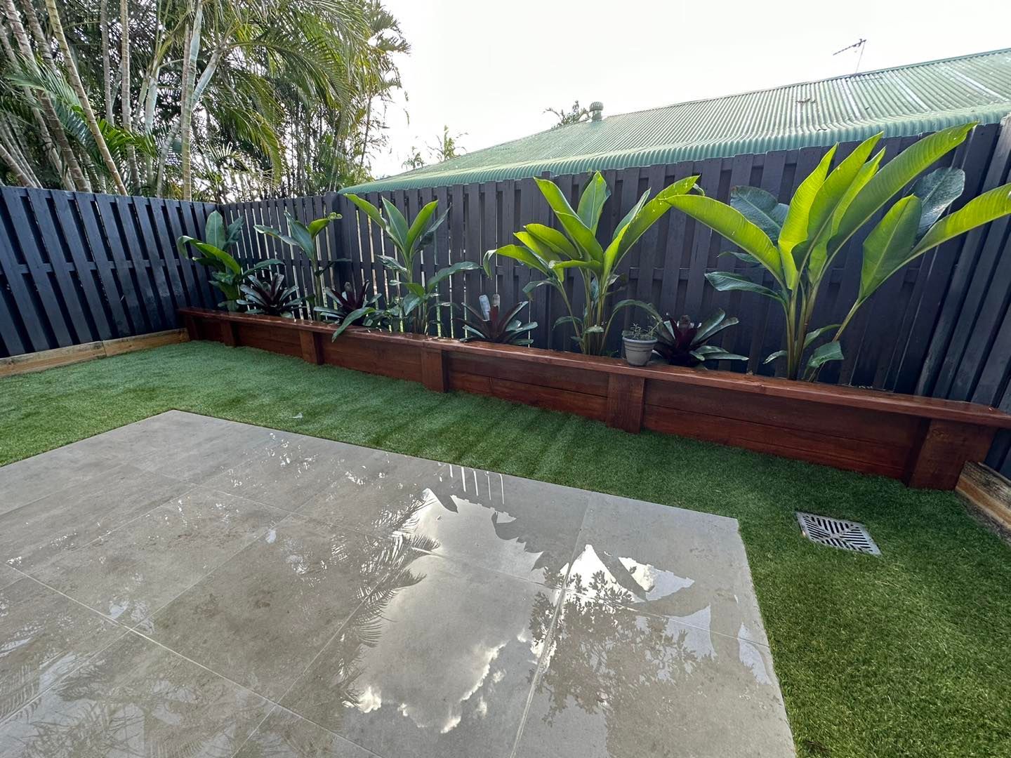 A backyard with a fence , grass , and plants. — Turnscape Landscaping in Beechmont, QLD