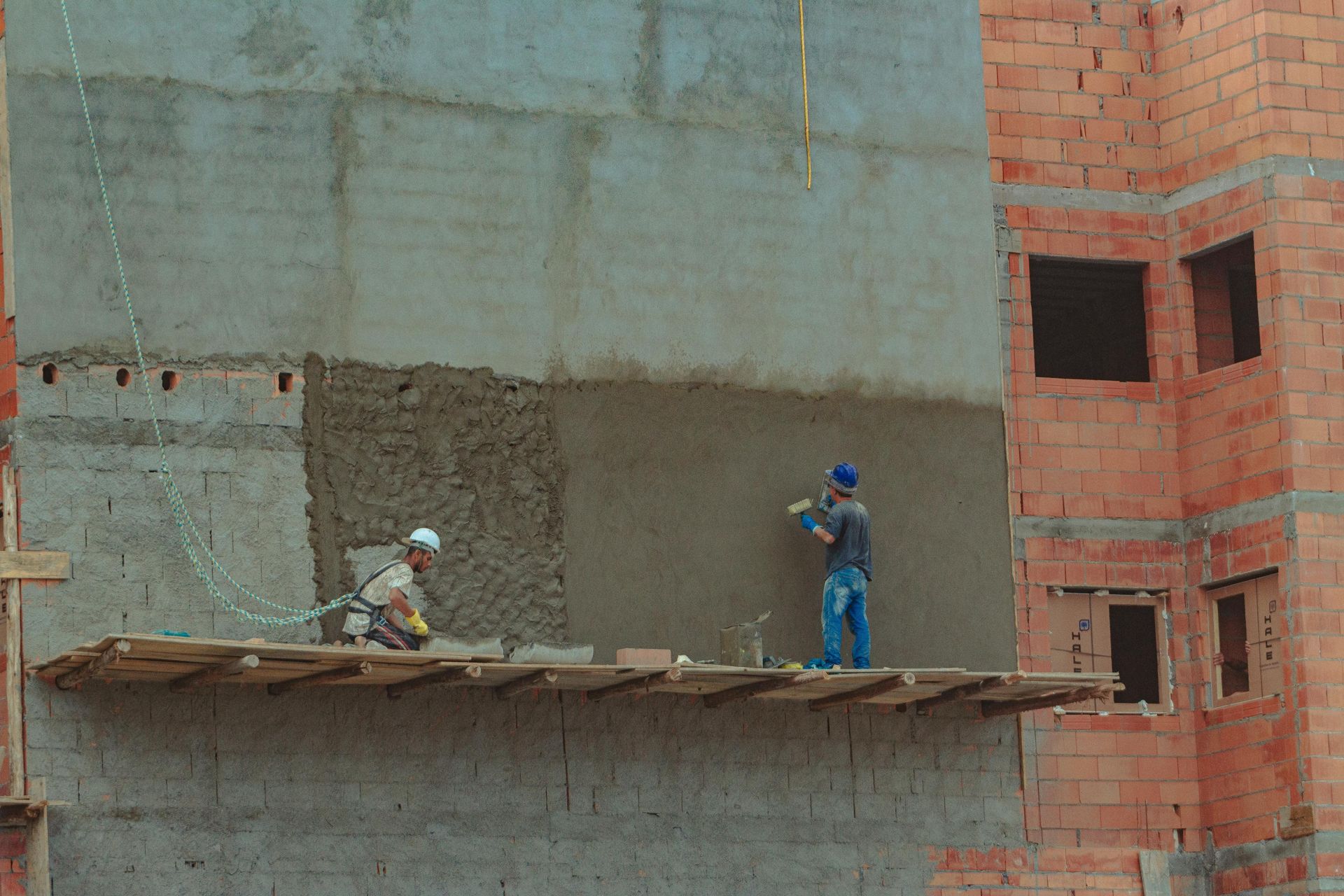 Two construction workers are working on the side of a building.