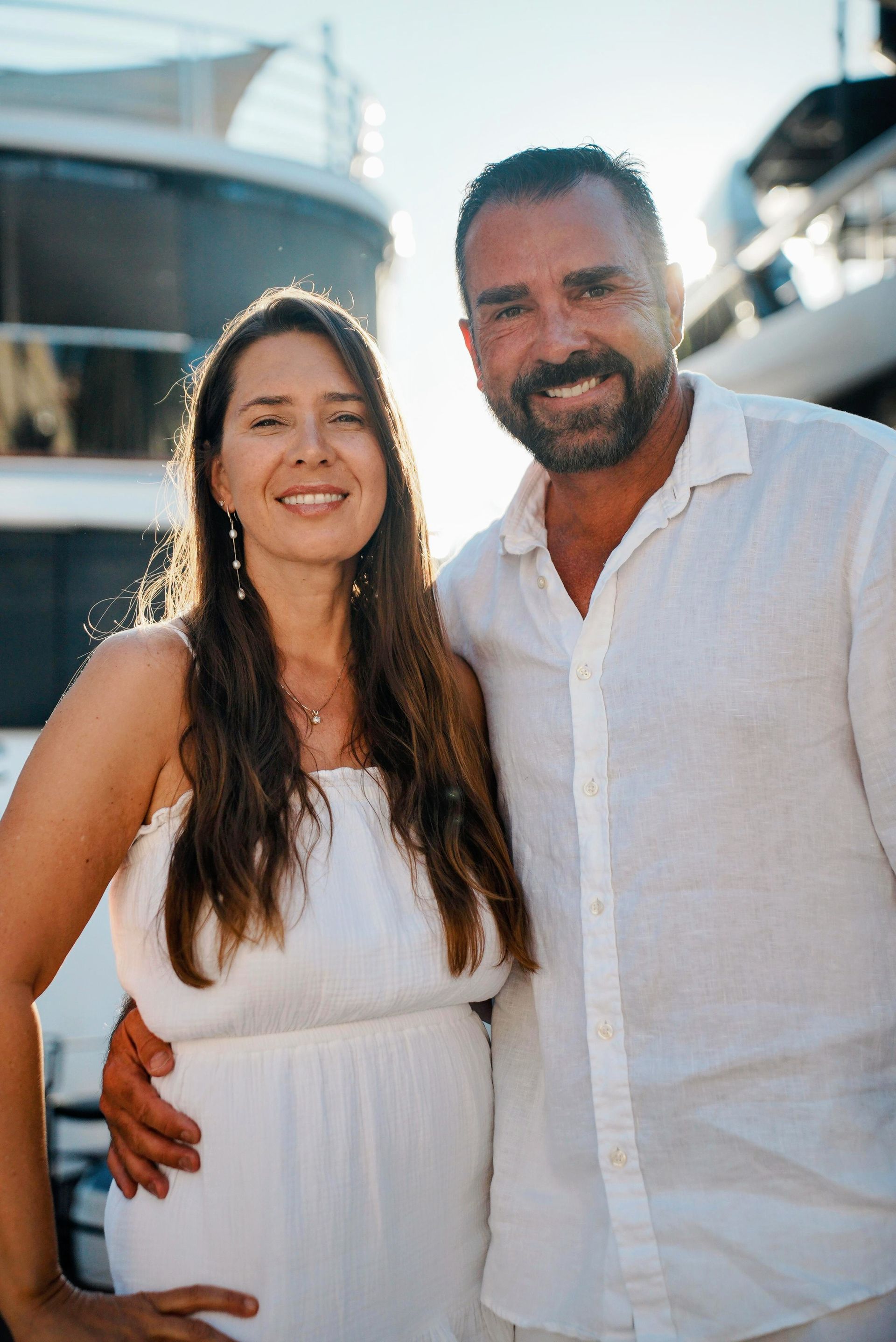 Woman and man posing indoors; she wears black top, silver pants, and he wears a silver suit.