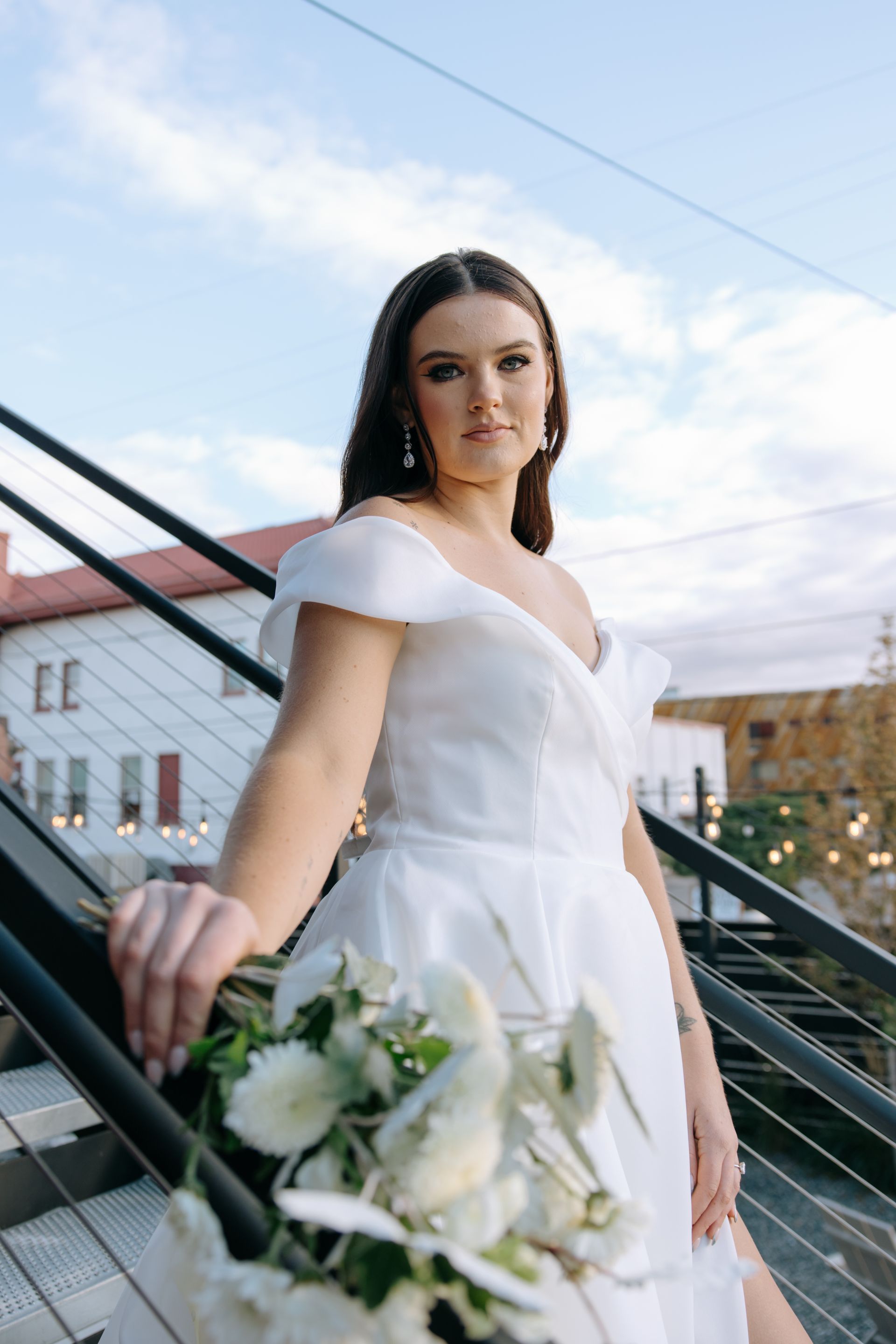 Bride in a white dress holding a bouquet on an outdoor staircase with a blue sky background