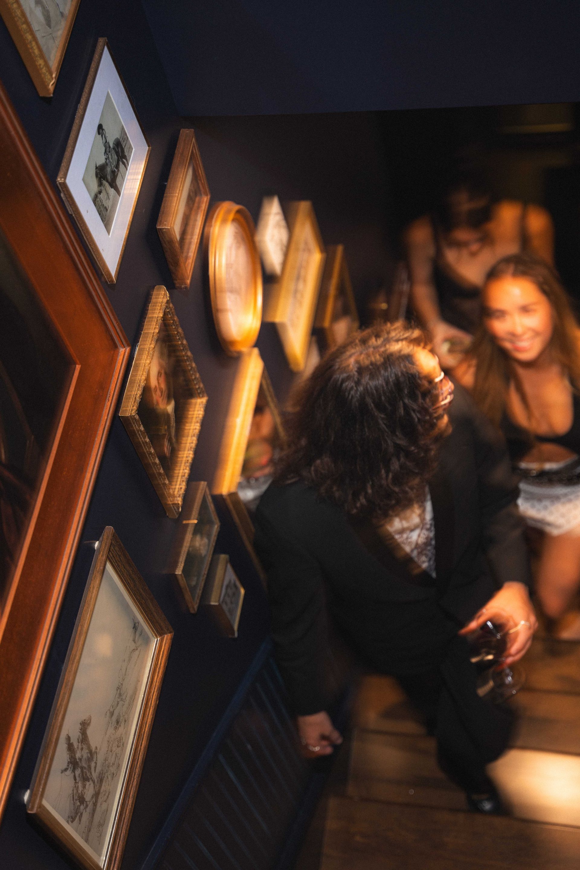 Dimly lit staircase with framed photos on the wall and people descending inside a house or venue
