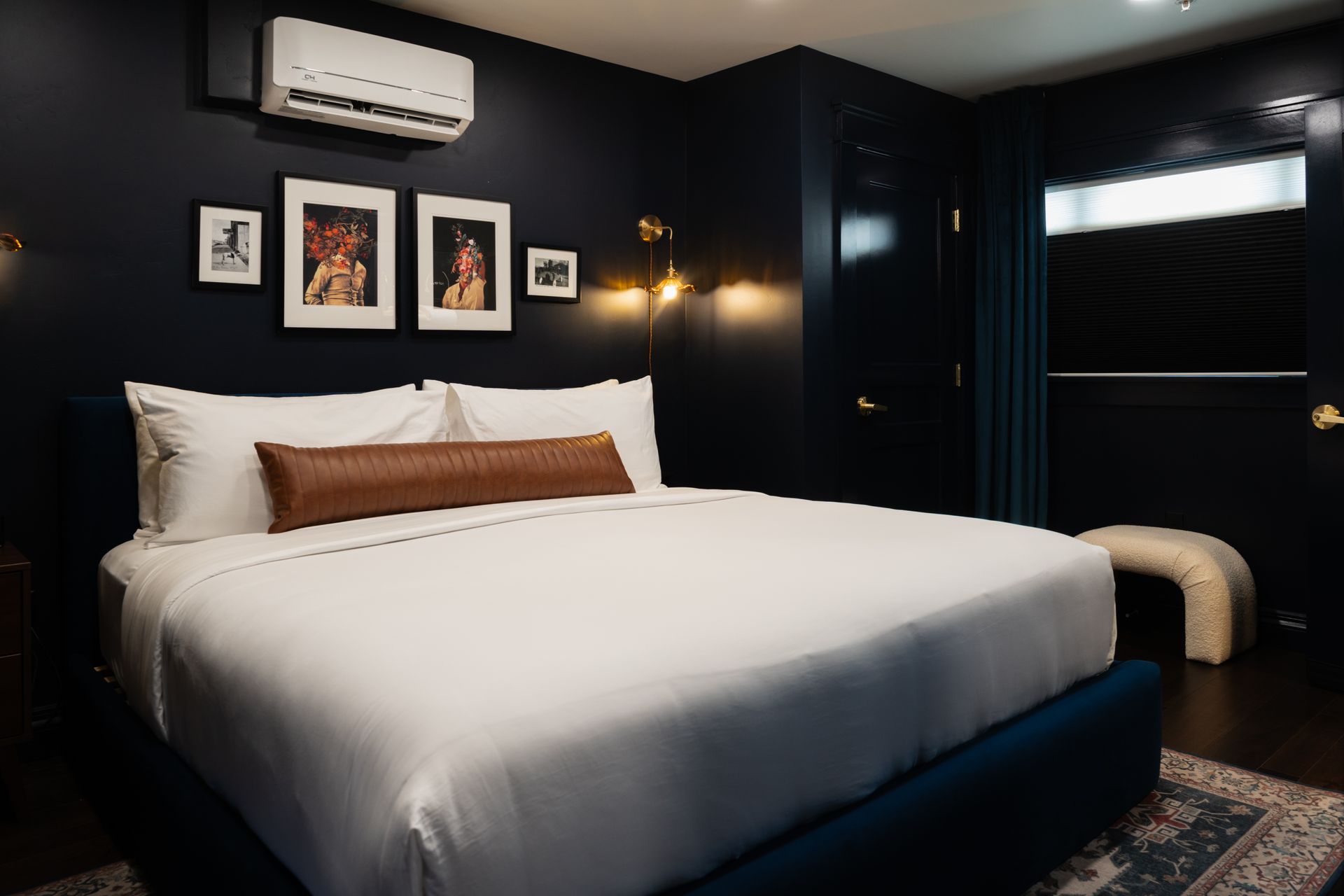 Stylish dark bedroom with a large white bed, framed wall art, and an air conditioner above the headboard