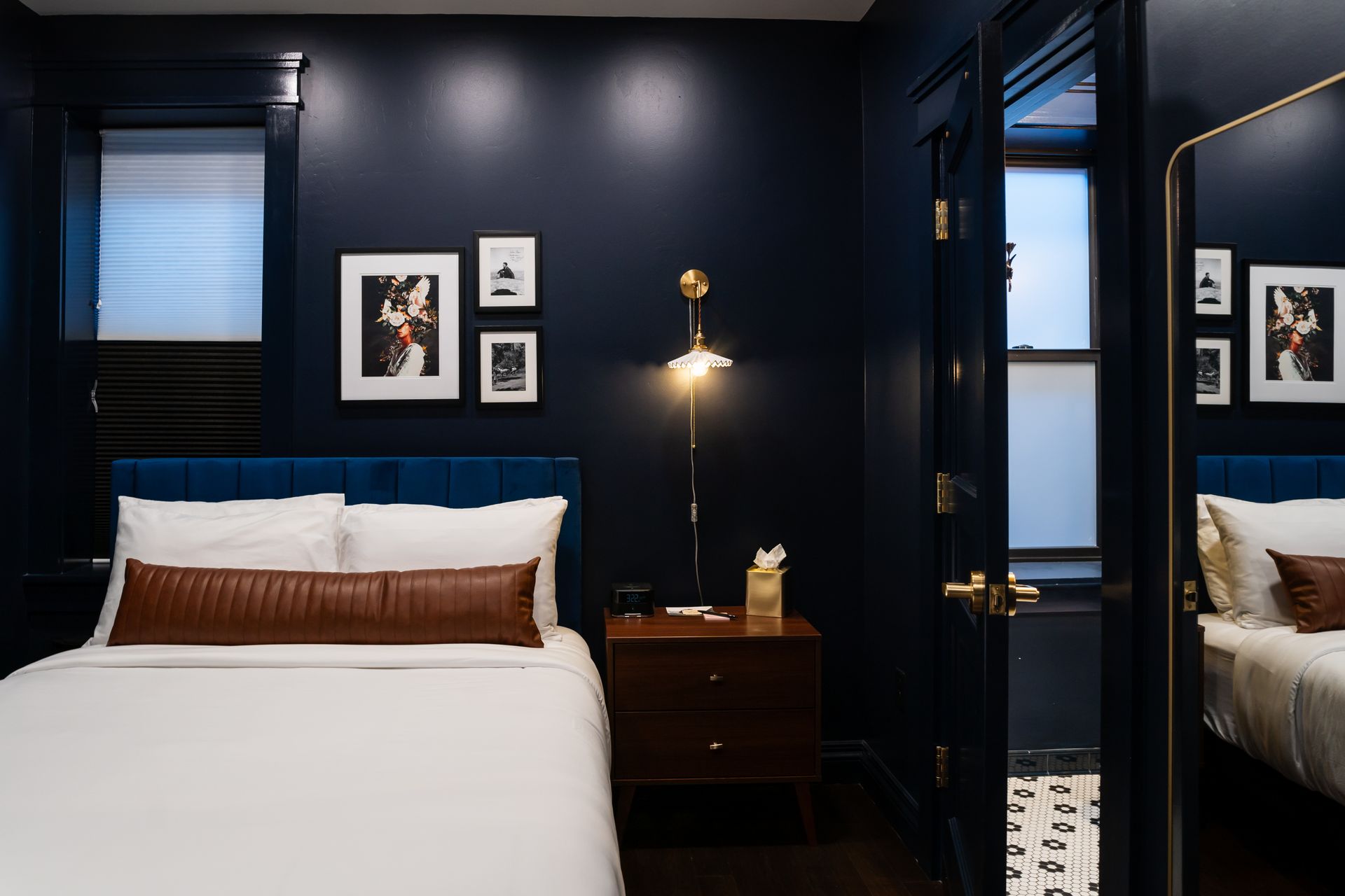 Dark navy bedroom with a white bed, framed wall art, and a mirrored closet door.