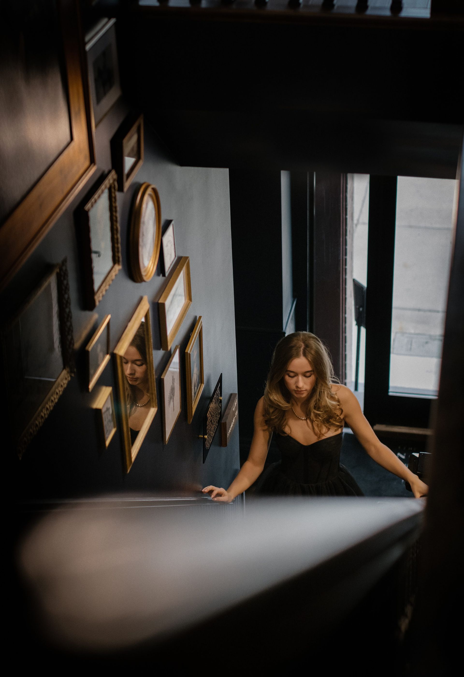 Woman climbing a narrow stairwell beside a wall of framed portraits