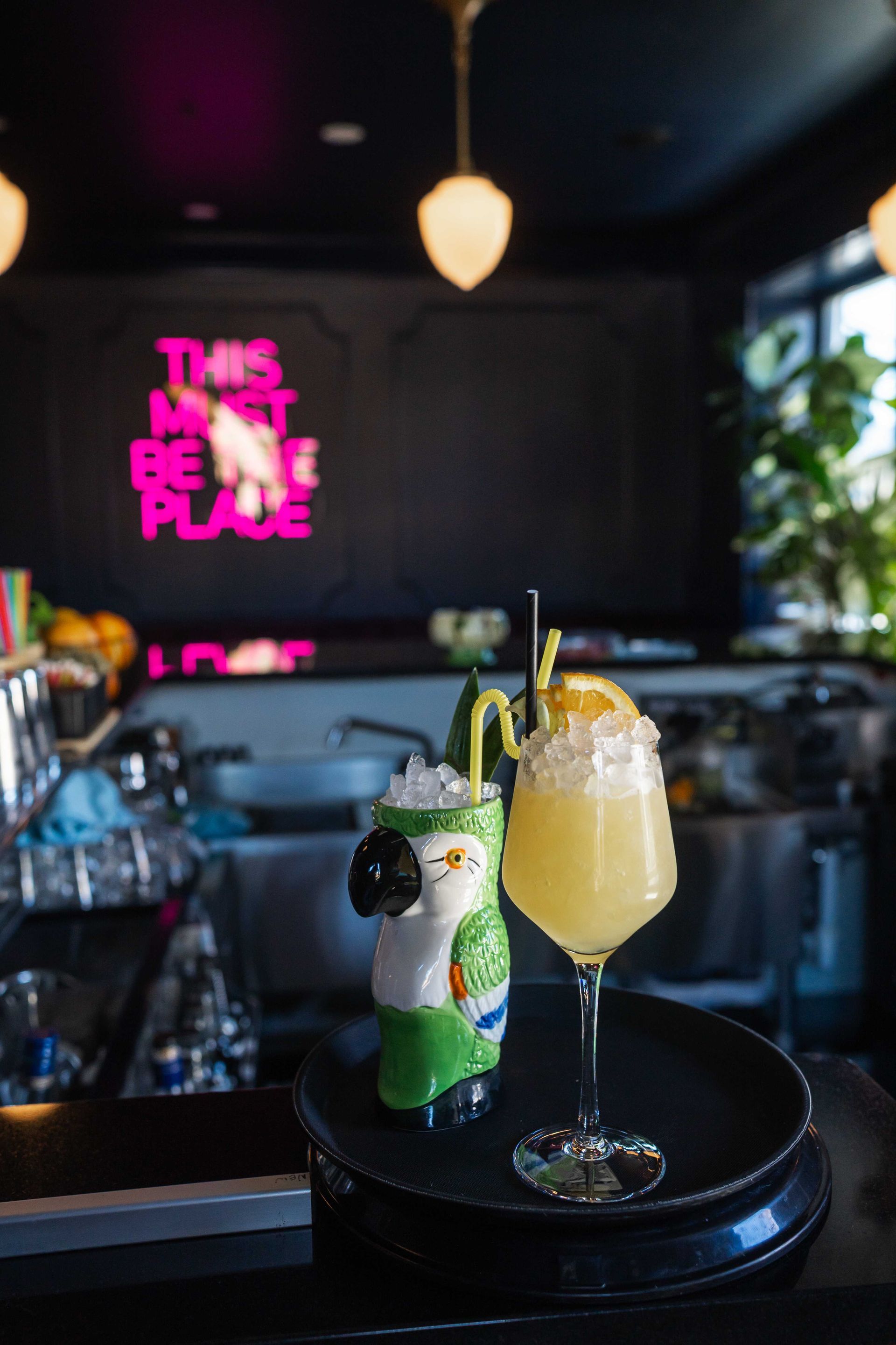 Cocktail and small pineapple garnish on a tray in a dimly lit neon bar interior