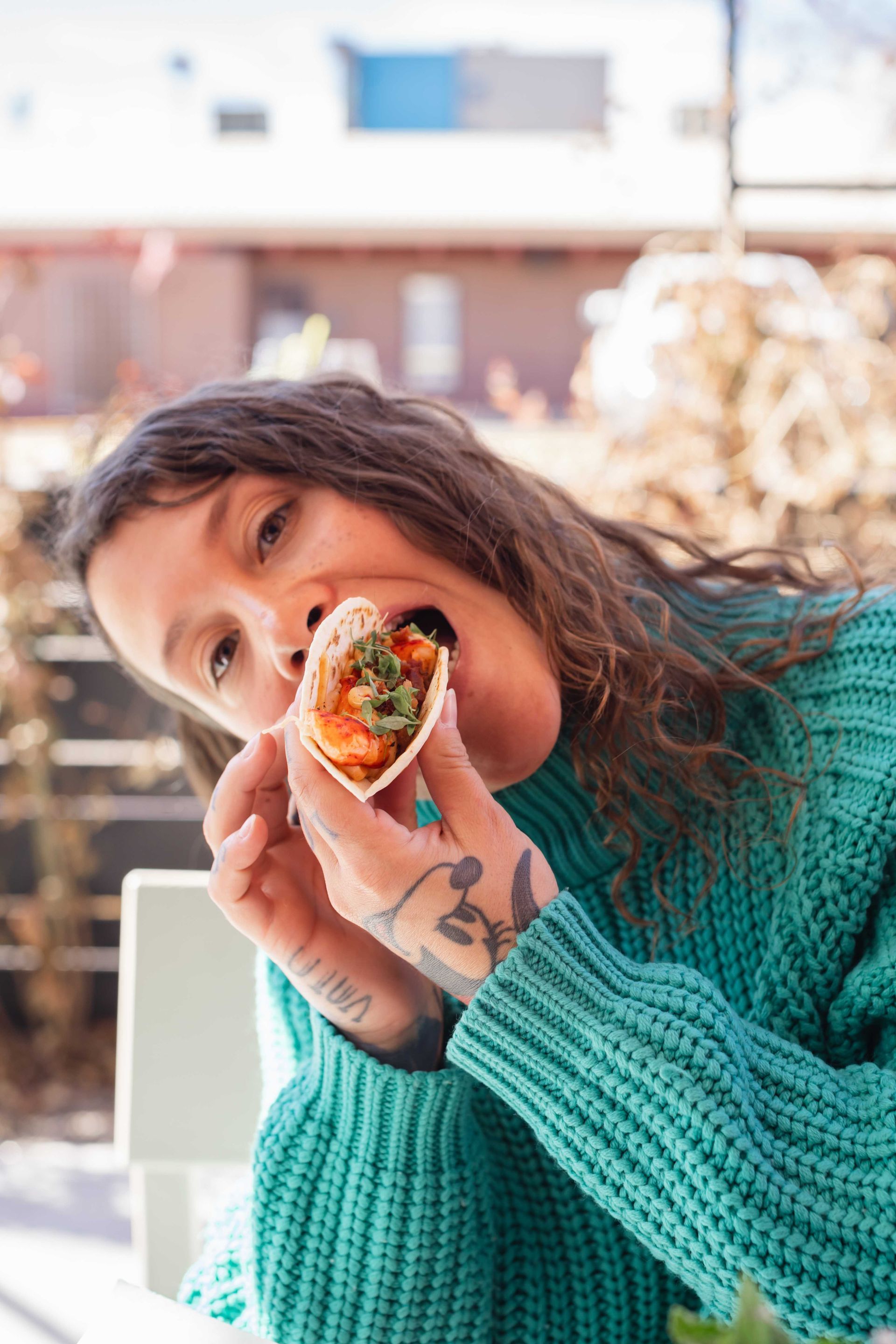 Woman in a teal sweater taking a bite from a wrapped burrito outdoors