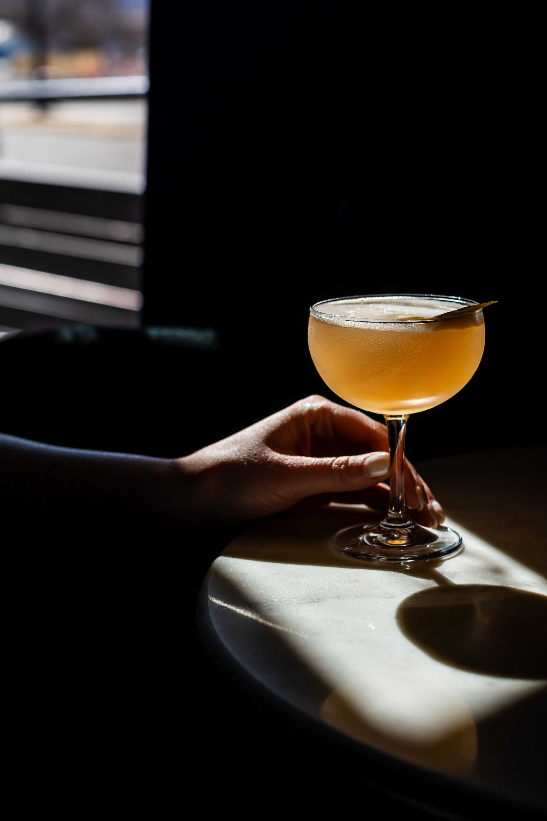 Hand holding a stemmed cocktail glass with a golden drink in sunlight