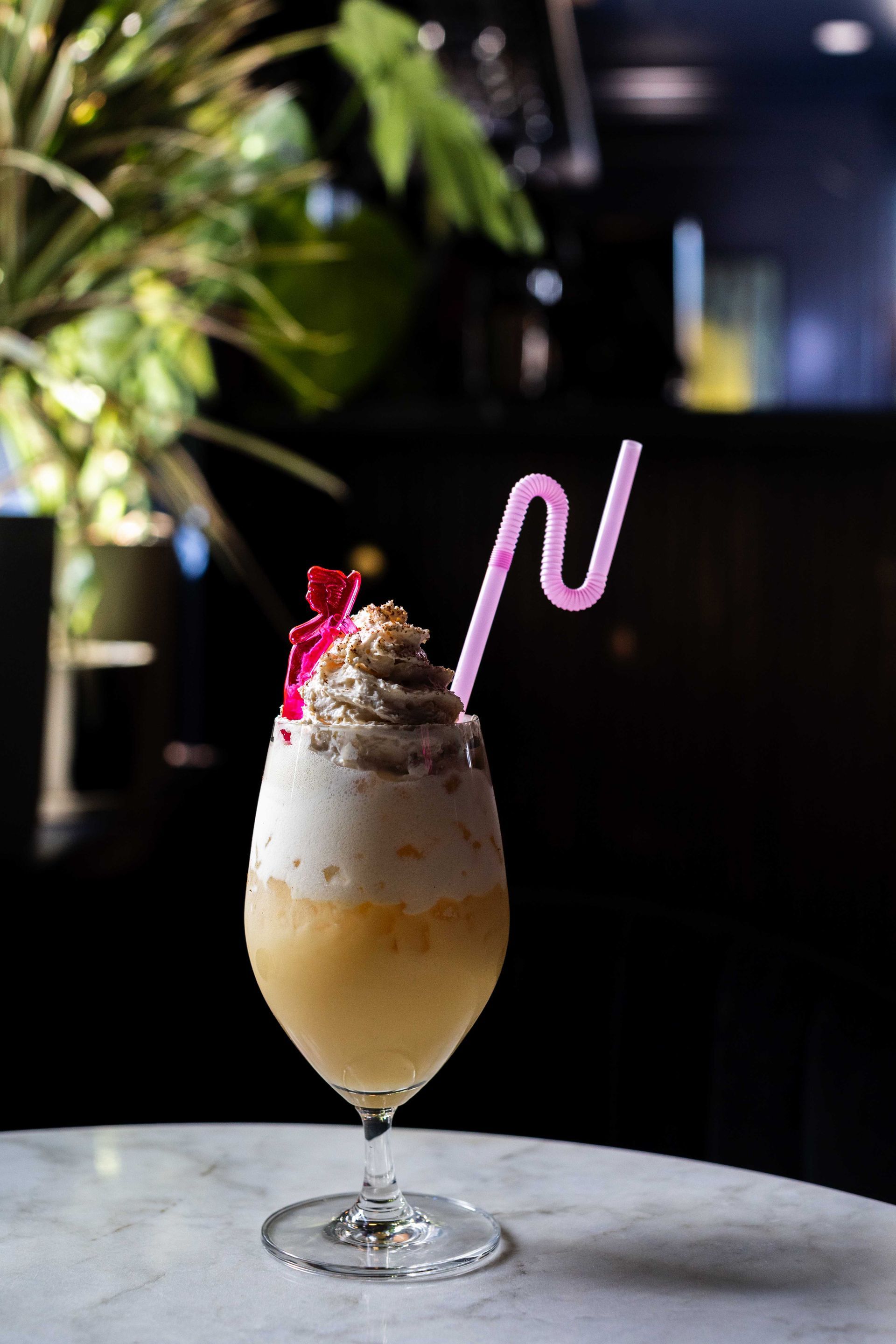 Pink cocktail with cream and cherry garnish in a stemmed glass on a marble table