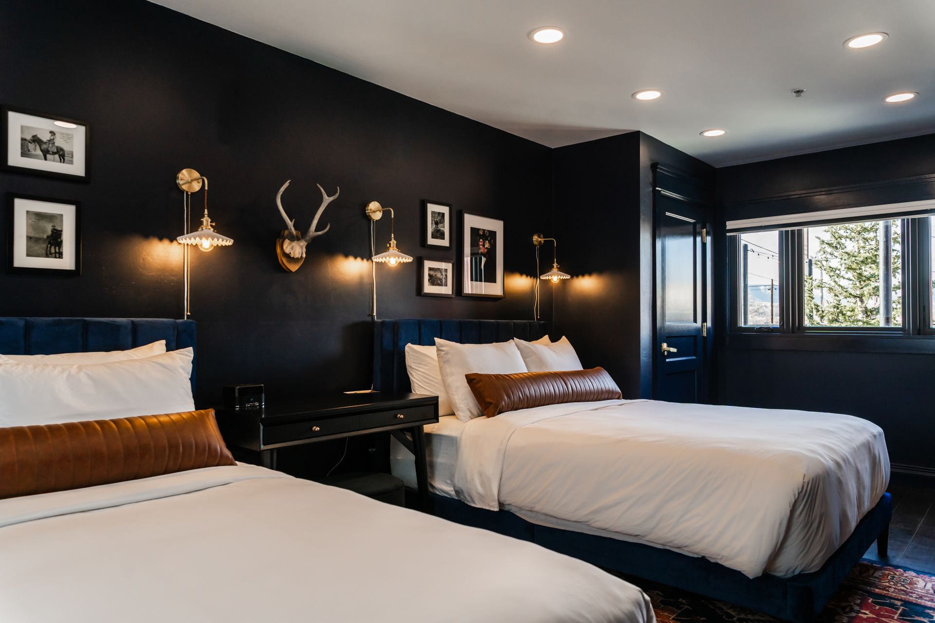 Modern bedroom with two beds, black walls, white bedding, and framed wall art under warm lights
