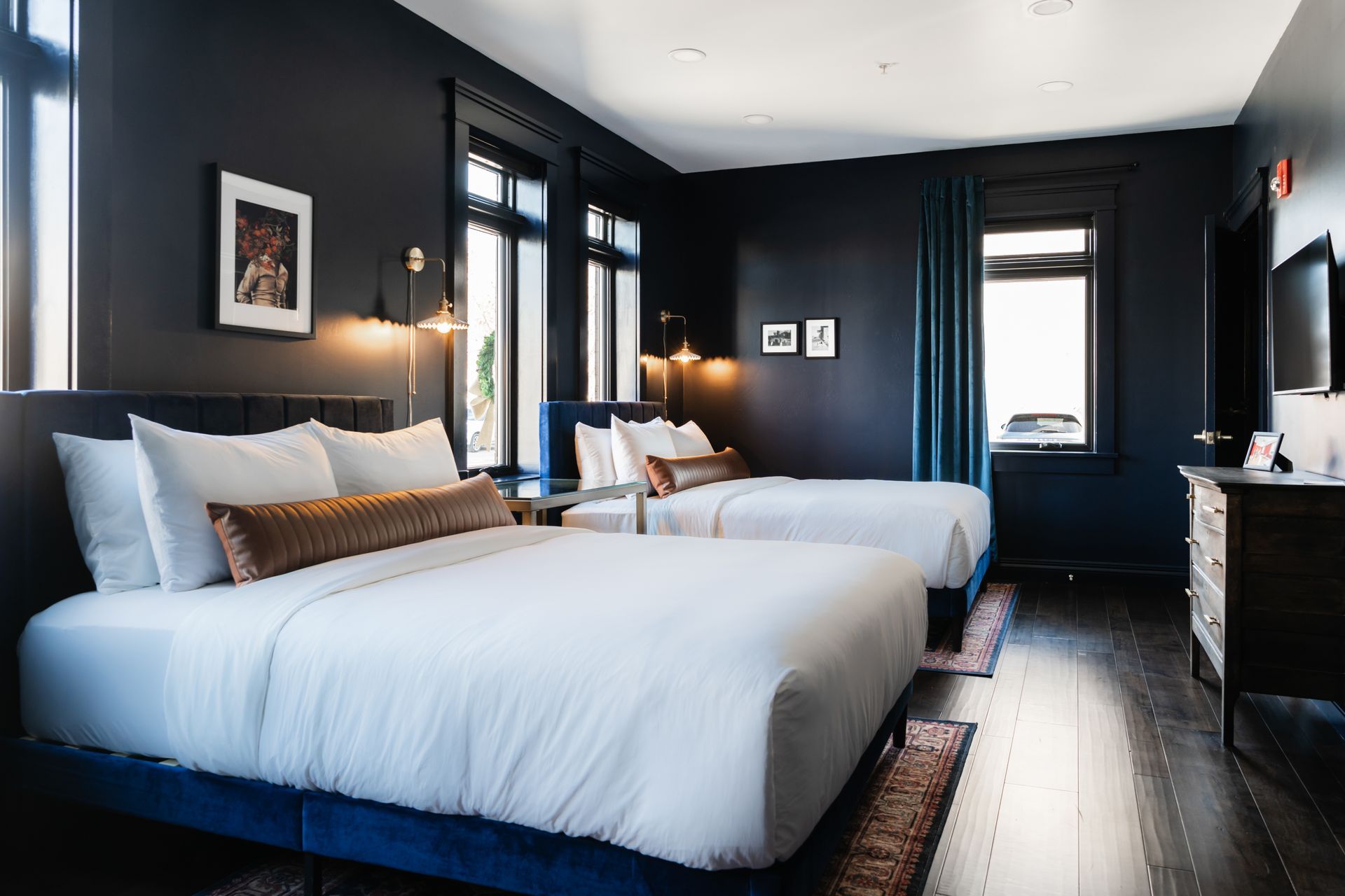 Modern hotel room with two white beds, dark walls, and large windows