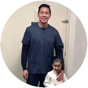 A man in scrubs is standing next to a little girl in a room.