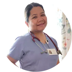 A woman in a blue scrub top with a stethoscope around her neck is smiling.