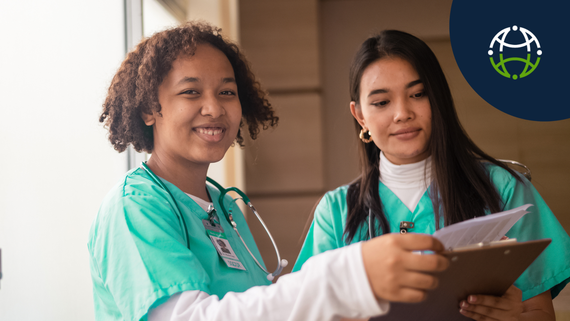 Two nurses, one smiling at the camera and the other looking down at a clipboard. 