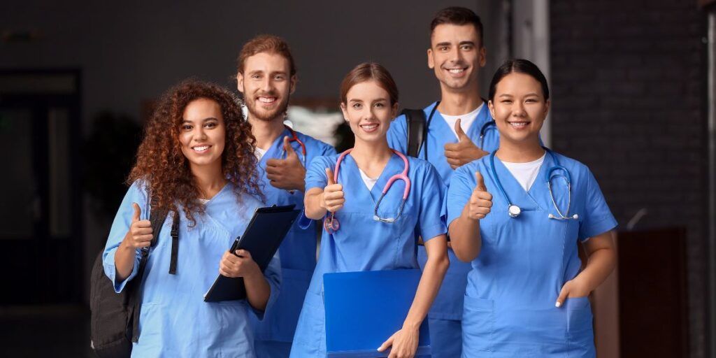 A group of medical students are standing next to each other and giving a thumbs up.