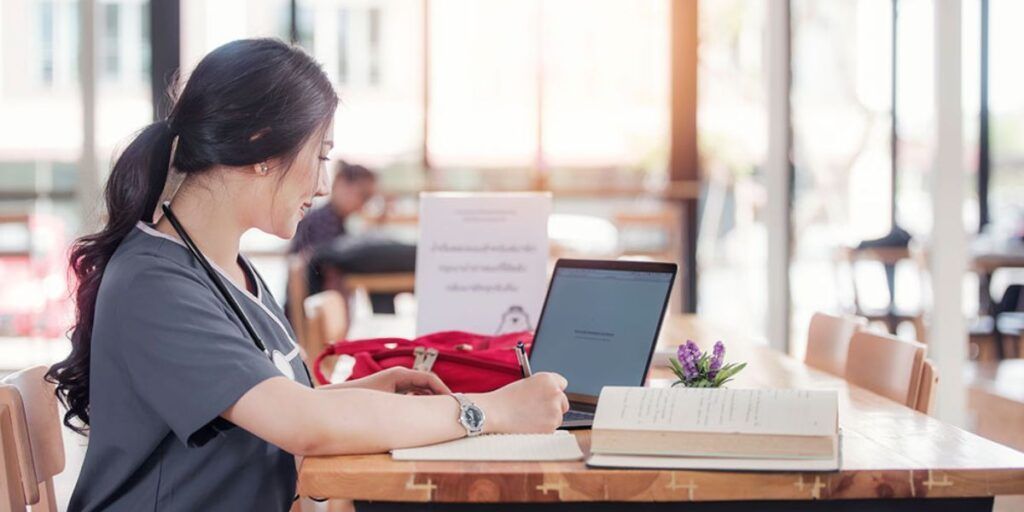 A nurse is sitting at a table using a laptop computer.