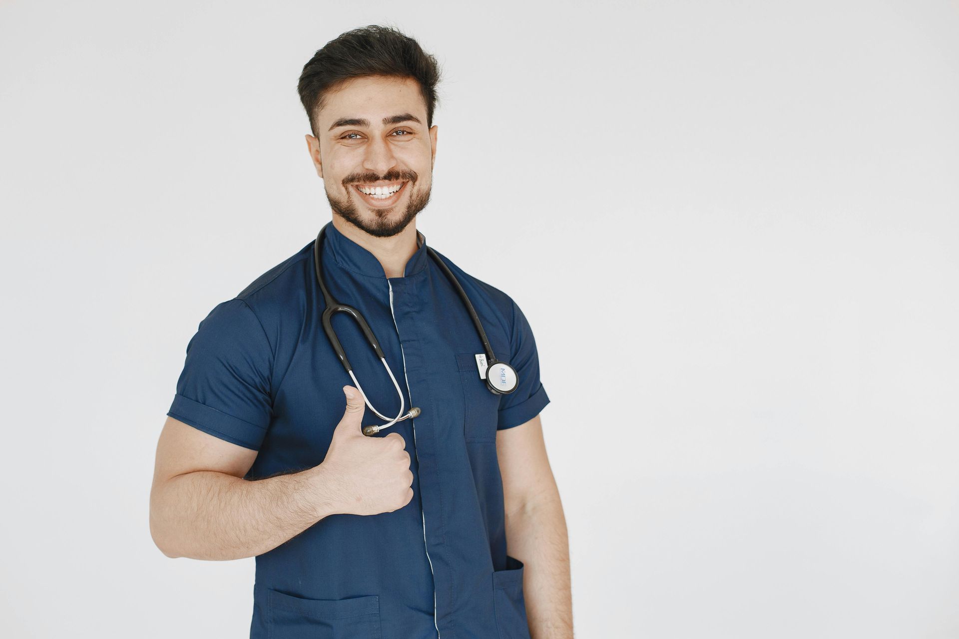 A doctor with a stethoscope around his neck is giving a thumbs up.