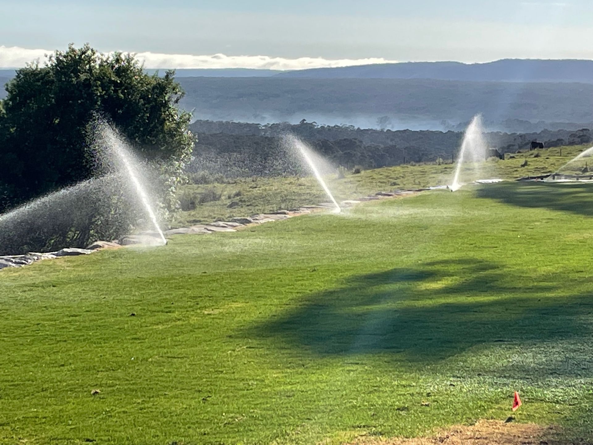 A row of sprinklers are spraying water on a lush green field- Irrigation Solutions in Southern Highlands, NSW