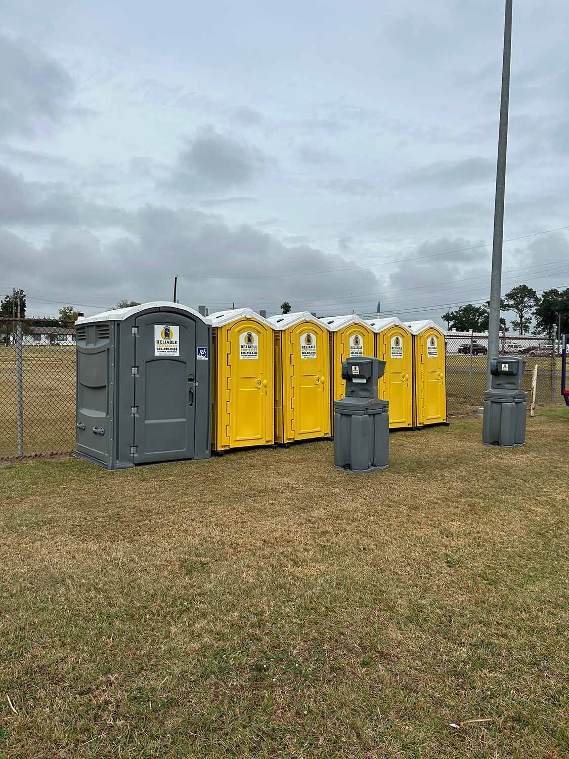 A row of portable toilets are lined up in a field.