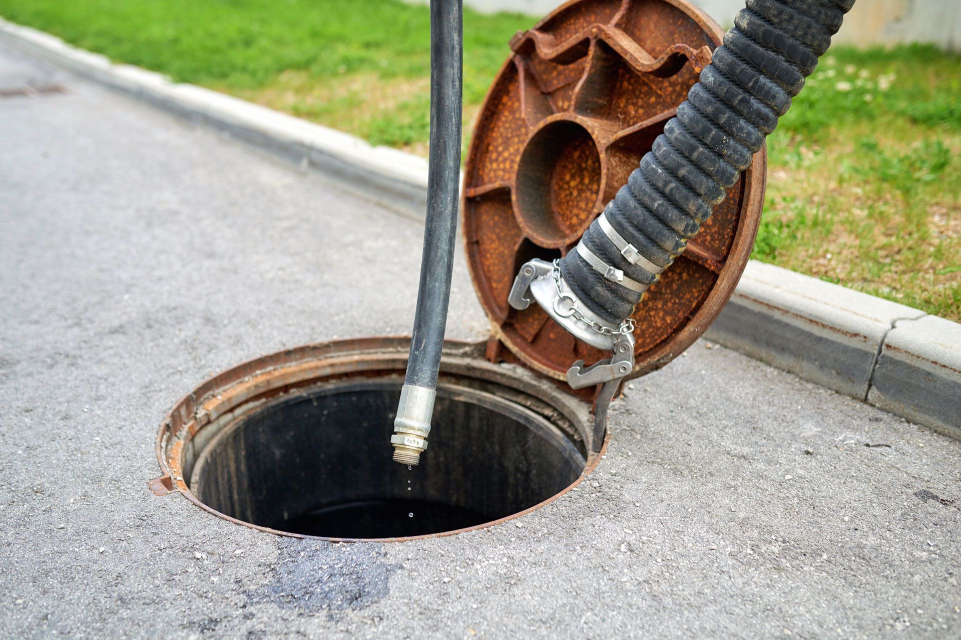 A manhole cover is open and a hose is coming out of it.