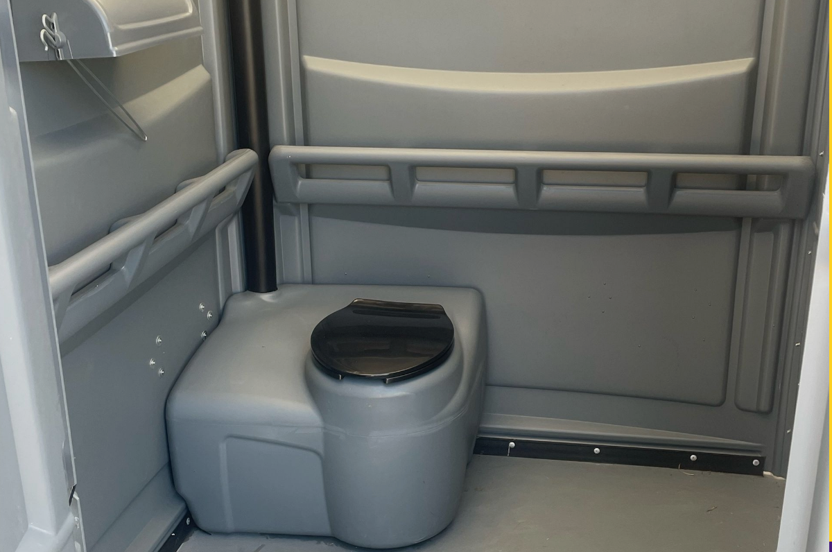 A toilet with a black seat is in a portable toilet
