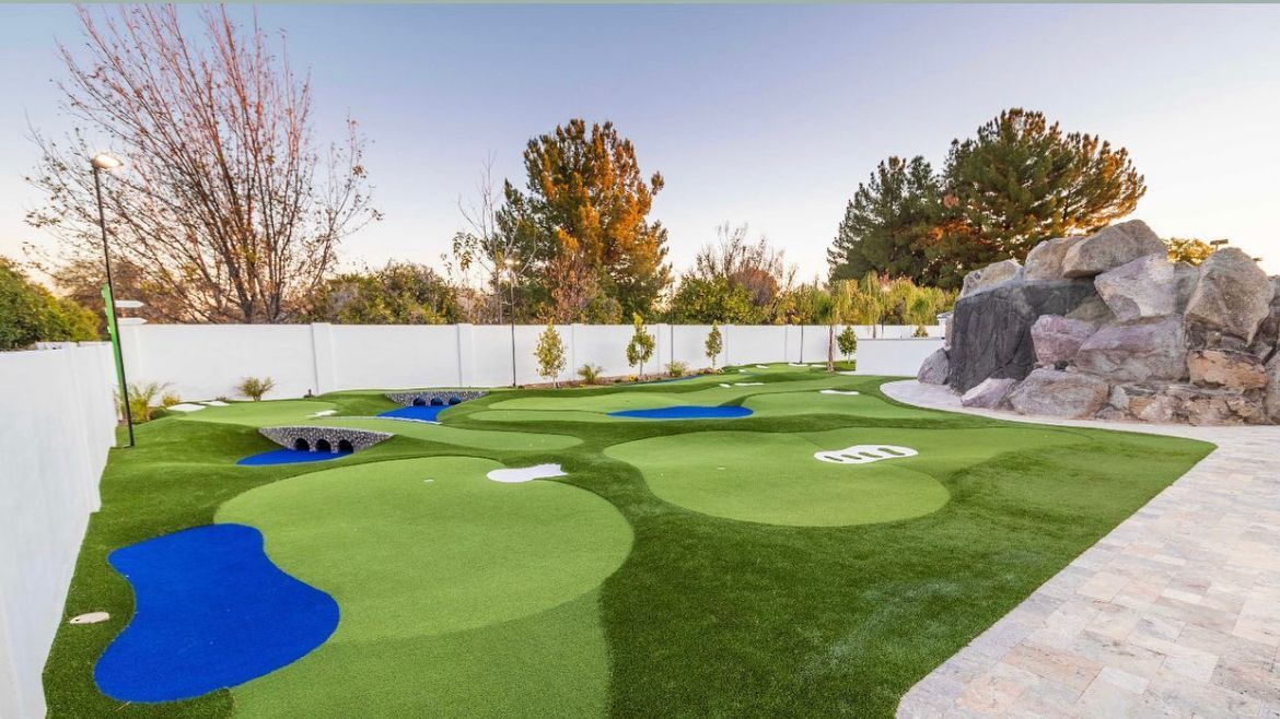 a mini golf course with a white fence and trees in the background