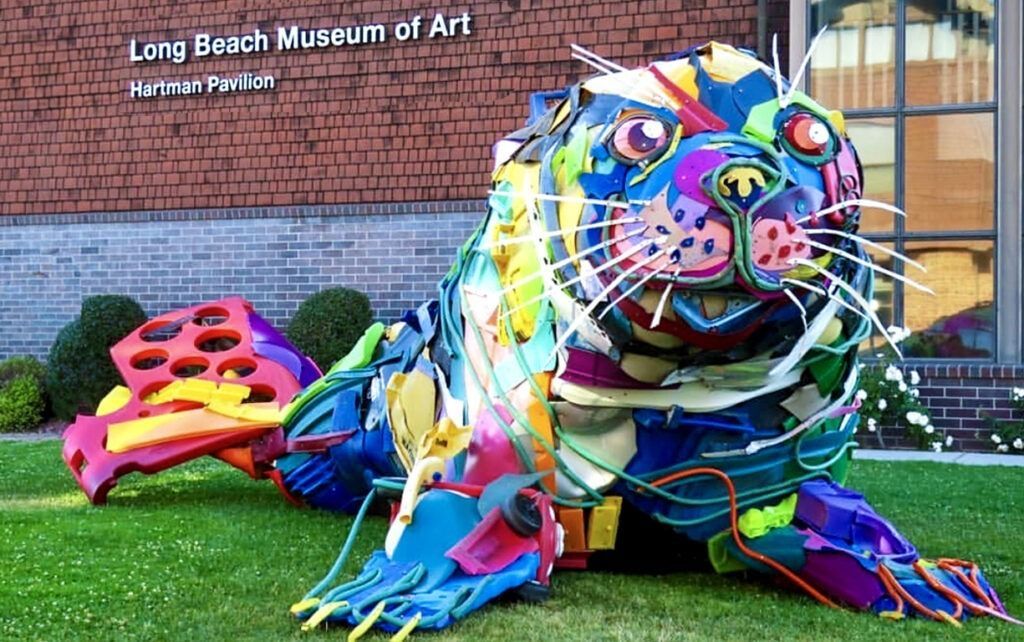 A colorful seal made out of plastic bottles is sitting on the grass in front of the long beach museum of art.