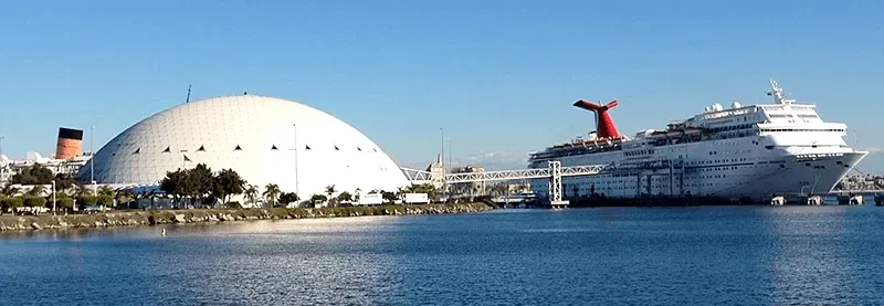 A large cruise ship is docked next to a large dome in the water.