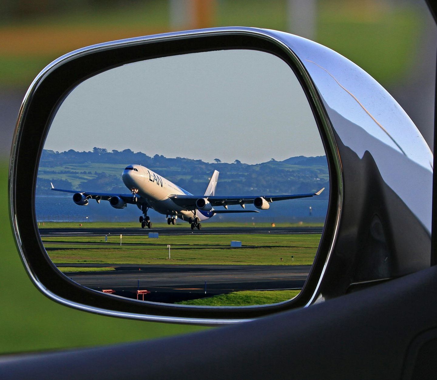 A rear view mirror shows an airplane taking off from an airport