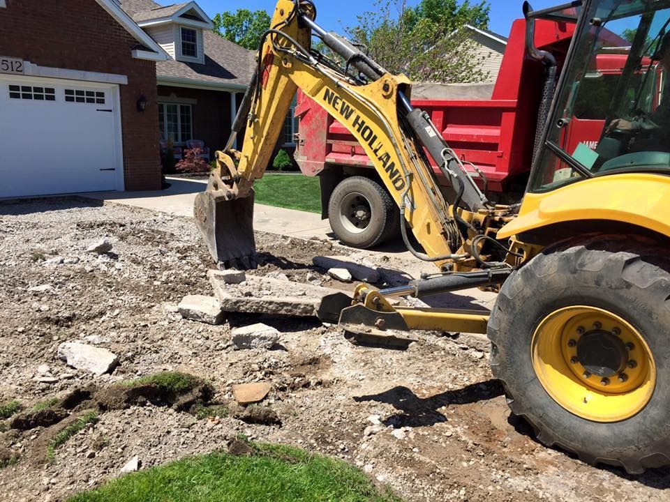 Yellow backhoe loading debris into a red dump truck on a driveway.