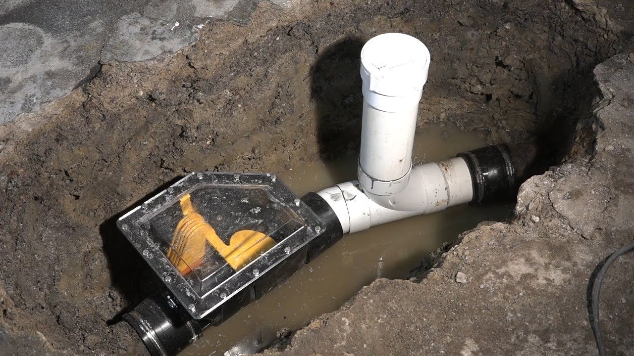 A partially buried black water pipe with a red valve, connected with black fittings, in a muddy excavation.