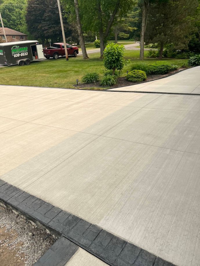 A concrete driveway with a newly paved section; a green portable toilet is in the background.